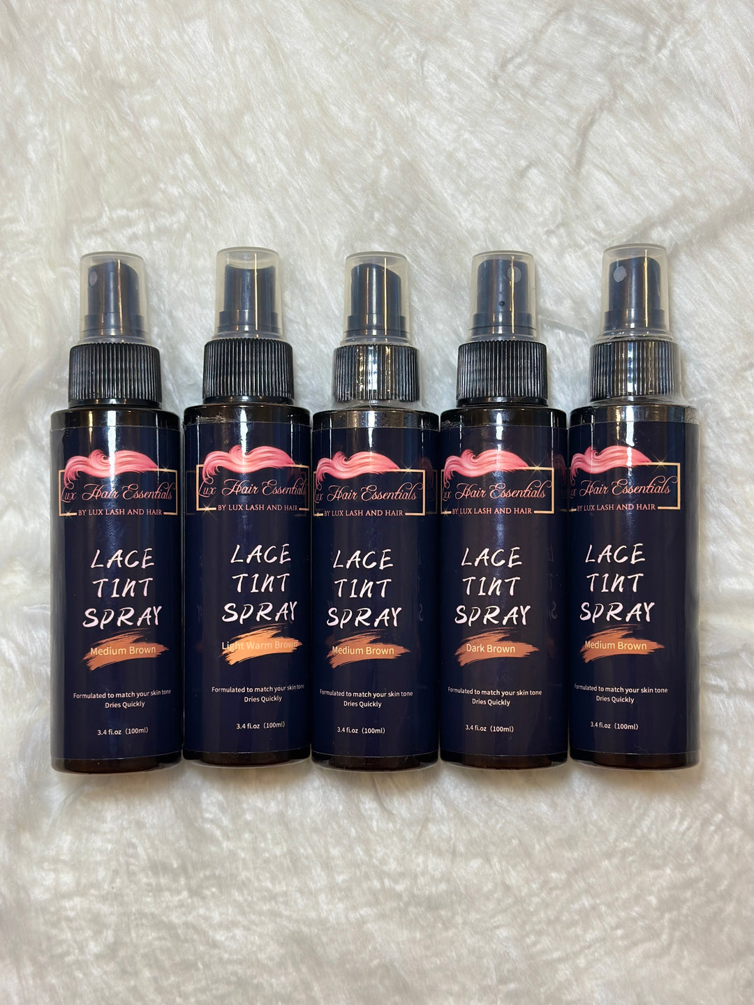 Five bottles of Lux Hair Essentials Lace Tint Spray in different shades displayed on a soft white background.
