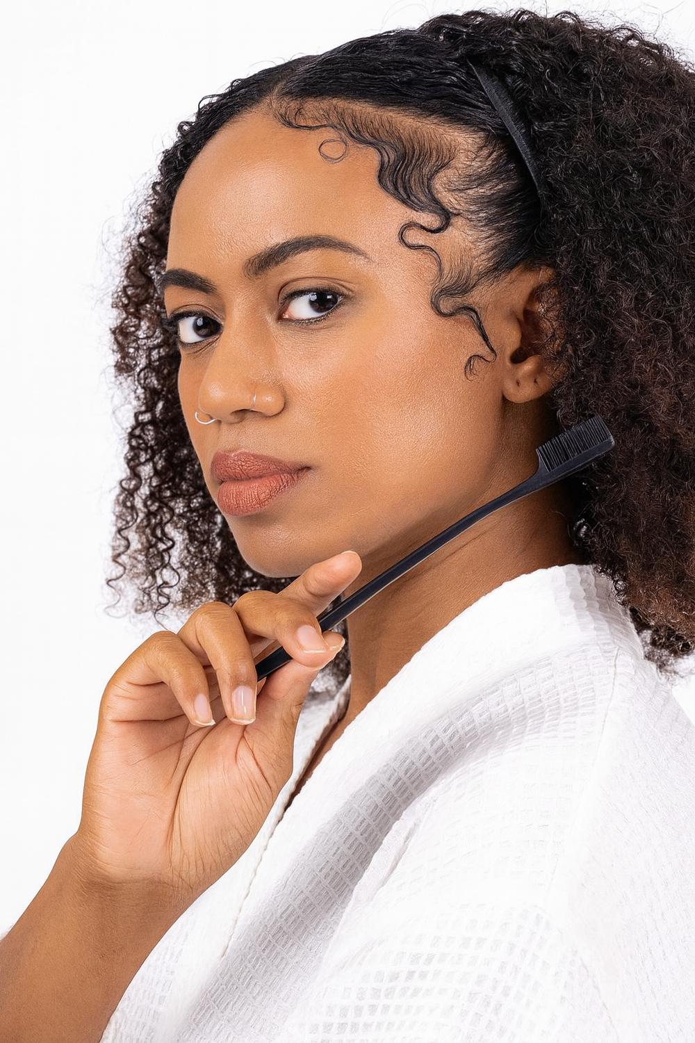 Model with sleek baby hairs using Lux Lash and Hair edge brush, natural curly hair, white robe, on white background.