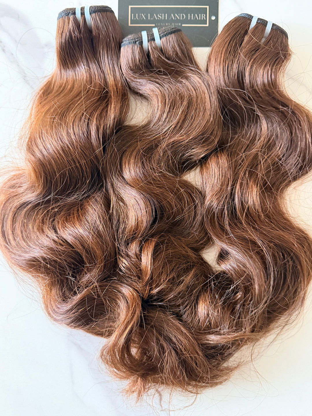 Lux Lash and Hair Brown Sugar Luxe natural wave 3-bundle set in 16” and 18” lengths displayed on marble background.