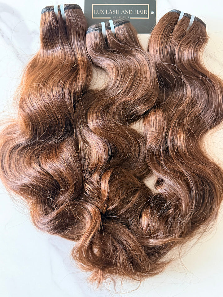 Lux Lash and Hair Brown Sugar Luxe natural wave 3-bundle set in 16” and 18” lengths displayed on marble background.