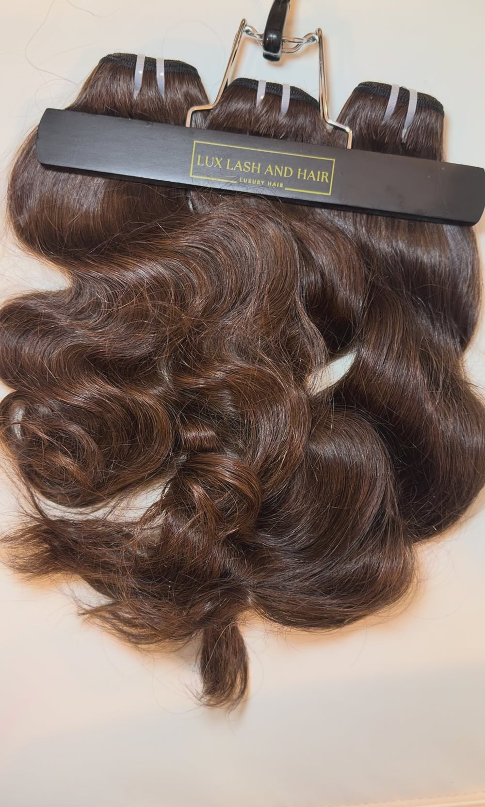 Video of Lux Lash and Hair Brown Sugar Luxe natural wave 3-bundle set in 16” and 18” lengths displayed on marble background.