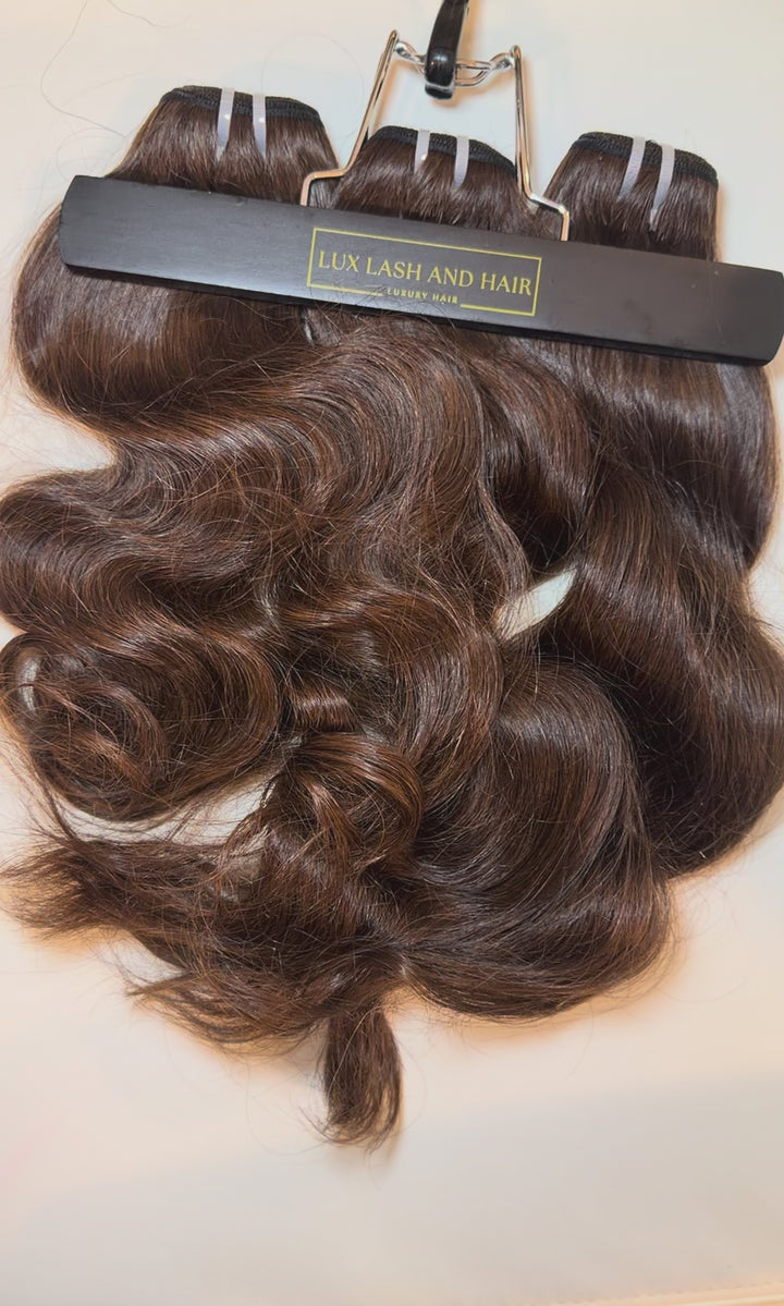 Video of Lux Lash and Hair Brown Sugar Luxe natural wave 3-bundle set in 16” and 18” lengths displayed on marble background.